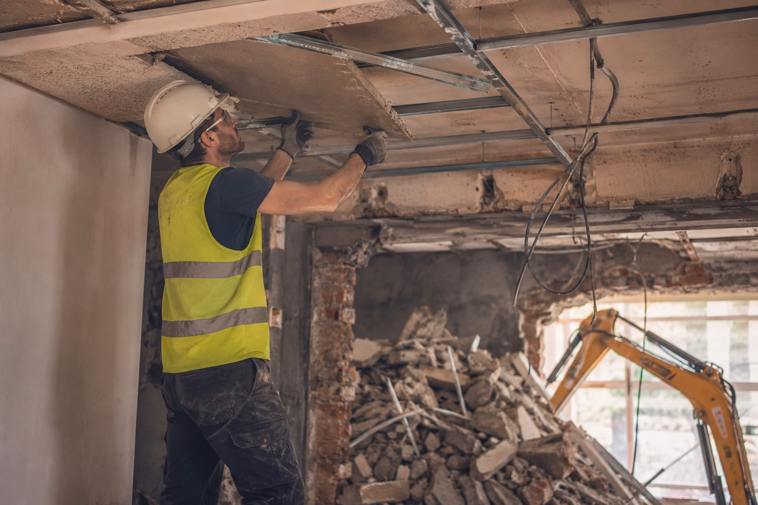Ouvrier en EPI démontant un plafond suspendu en dalles minérales dans un appartement toulousain en rénovation