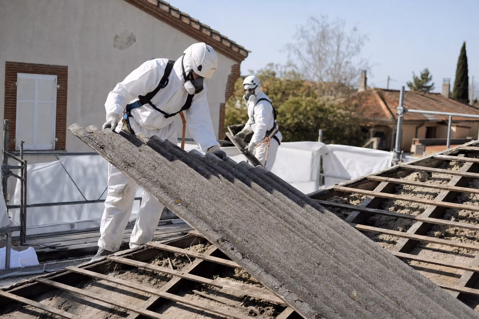 Ouvrier en combinaison de protection retirant une toiture en fibrociment amianté sur un chantier près de Toulouse